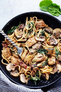 a skillet filled with pasta, mushrooms and spinach on top of a table