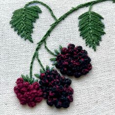 two crocheted flowers on a piece of cloth with green leaves and red berries