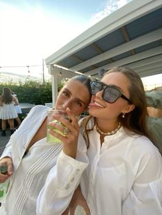 two women are drinking from glasses at an outdoor event