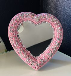 a pink heart shaped mirror sitting on top of a table