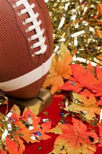 an american football sitting on top of a pile of leaves next to gold and red confetti