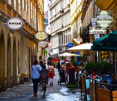 people walking and riding bicycles down an alleyway with shops on both sides in the city