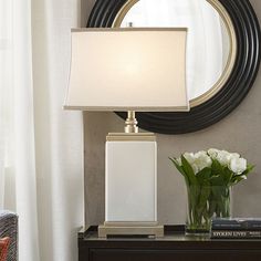 a table with a lamp and some flowers on it next to a mirror in the corner