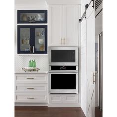 two microwaves are built into the wall in this kitchen with white cabinets and dark wood floors