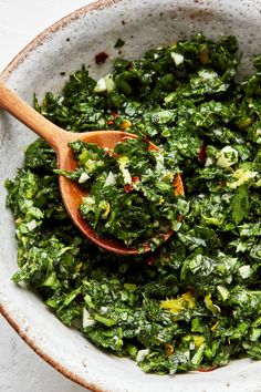 a wooden spoon in a bowl filled with greens