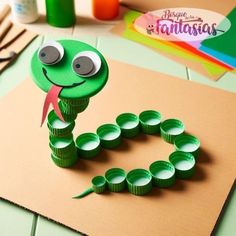 a green snake made out of toilet paper on top of a table next to craft supplies