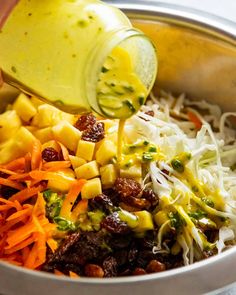 someone pouring dressing into a bowl filled with vegetables and pasta salad ingredients, including carrots, broccoli, shredded cheese, raisin sprinkled with parmesan