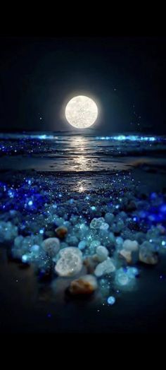 the full moon shines brightly in the night sky over water and rocks on the beach