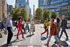 several people crossing the street in front of tall buildings on a sunny day with skyscrapers in the background