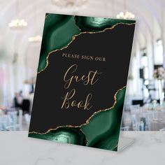 a black and gold guest book sitting on top of a white table with chairs in the background