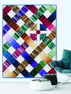 a colorful quilt hanging on the wall next to a chair and ottoman in front of it