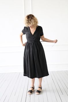 a woman in a black dress stands on a white floor with her back to the camera