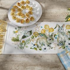 the table runner has an image of two rabbits on it and is next to a plate with muffins