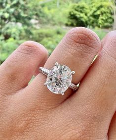 a woman's hand with a diamond ring on top of her finger and trees in the background