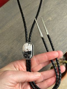 A leather braided cord in black with a cushion cut White Buffalo set in sterling silver. The bolo cord length is 22 inches when held taught, folded. It has sterling silver tips. The "pendant" moves easily enough along the cord but is also snug enough not to move unless given a tug. Tips are not glued on, but rather pinch the cord so it is not recommended to pull the tips while adjusting the "pendant." The setting measures 1-1/4 inches long. Suitable for men and women. Silver Lariat Jewelry With Adjustable Cord, Artisan Silver Jewelry With Adjustable Length, Handmade Sterling Silver Bolo Tie As Gift, Adjustable Silver Artisan Lariat Necklace, Adjustable Sterling Silver Lariat Bolo Tie, Silver Lariat Bolo Ties With Adjustable Length, Silver Lariat Bolo Tie With Adjustable Length, Adjustable Sterling Silver Bolo Tie For Gifts, Black Bolo Tie With Adjustable Cord As Gift