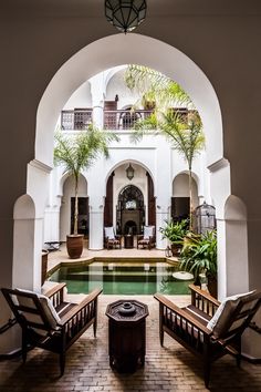 an indoor swimming pool with two chairs and a fire pit in the middle, surrounded by palm trees