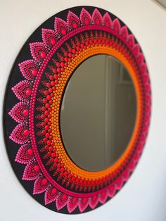 a round mirror with an orange and pink design on the front is hanging on a white wall