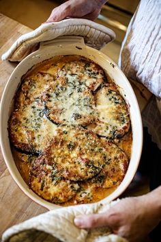 a person holding a casserole dish with spinach and cheese in it on a wooden table