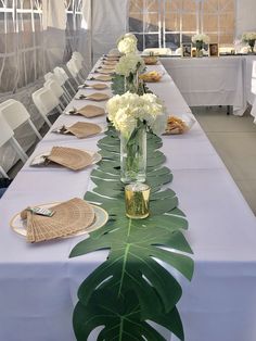 a long table with white flowers and greenery on it is set up for an event