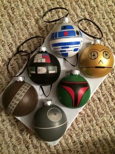 some star wars ornaments are sitting on a white plate with black cord and one has a red, green, blue, and silver helmet