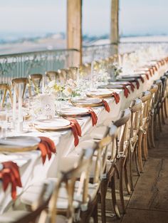 a long table with white plates and silverware is set up for an outdoor event