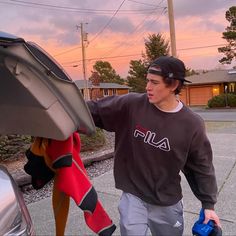 a young man walking towards a car with an umbrella on it's hood and another person holding a blue object in his hand