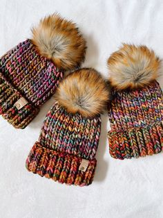 three knitted hats with fur pom - poms on top of each other