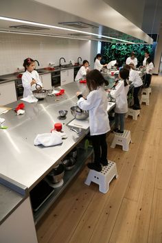 a group of people in white lab coats preparing food on top of metal counter tops