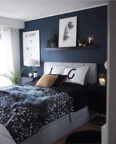 a bedroom with dark blue walls and white bedding, black comforter, two framed pictures on the wall