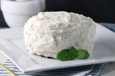 a white plate topped with a cake covered in frosting and green leaves next to a fork