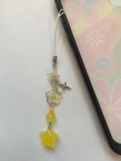 a cell phone with a yellow charm attached to it's side next to a pen