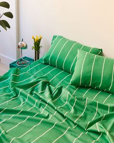 a bed with green sheets and pillows in a room next to a potted plant