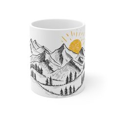 a white coffee mug with mountains and trees on the side, in front of a yellow sun