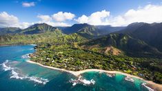 an aerial view of a tropical island with mountains in the background and blue water below