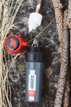 an orange and black flask next to a tree with some branches in the background