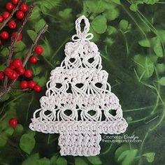 a crocheted christmas tree ornament on a green background with red berries