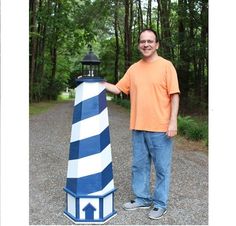 a man standing next to a blue and white light house in the middle of a forest