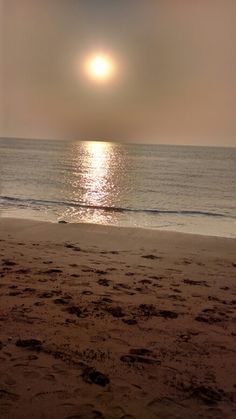 the sun is setting over the ocean and it's reflection in the water on the beach