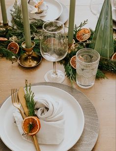 the table is set with silverware, orange slices and greenery on top of white plates