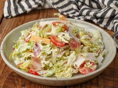 a white bowl filled with salad sitting on top of a wooden table next to a striped towel