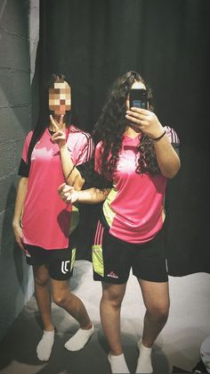 two women in pink shirts and black shorts are taking pictures with their cell phones while standing next to each other