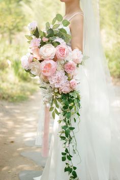 a bride holding a bouquet of pink roses and greenery on her wedding day in the woods