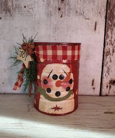 a tin can with a snowman painted on it and a ribbon around the top