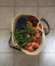 a basket filled with lots of fresh fruit on top of a tiled floor next to a handbag