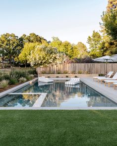 an outdoor pool with lawn chairs and umbrellas in the back yard, next to a wooden fence