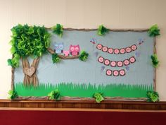 a bulletin board decorated with paper owls and green leaves on a mantle in front of a tree