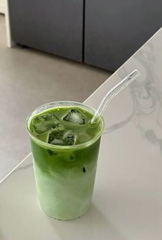 a green drink is sitting on a table with ice cubes and a straw in it