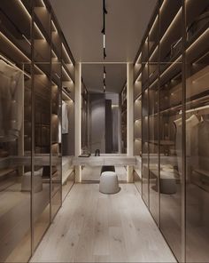 a large walk in closet with glass walls and wooden flooring, lighted by recessed lights