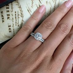 a woman's hand with a diamond ring on top of her finger and an old book in the background