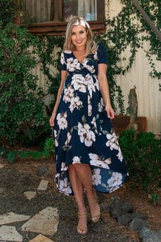 a woman standing in front of a house wearing a blue dress with white flowers on it